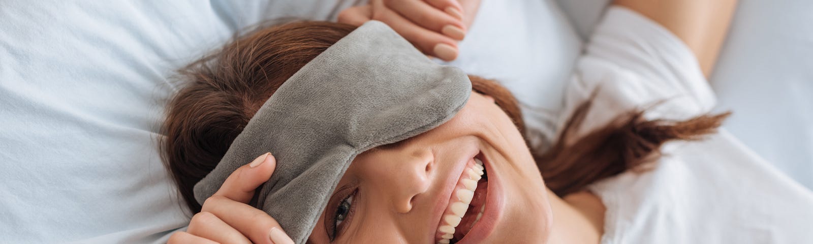 Overhead view of happy young woman in eye mask resting in bedroom