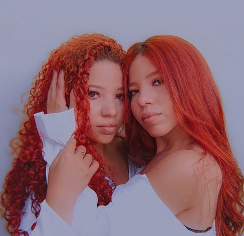 Two women, twin sisters, wear white shirts and long red hair