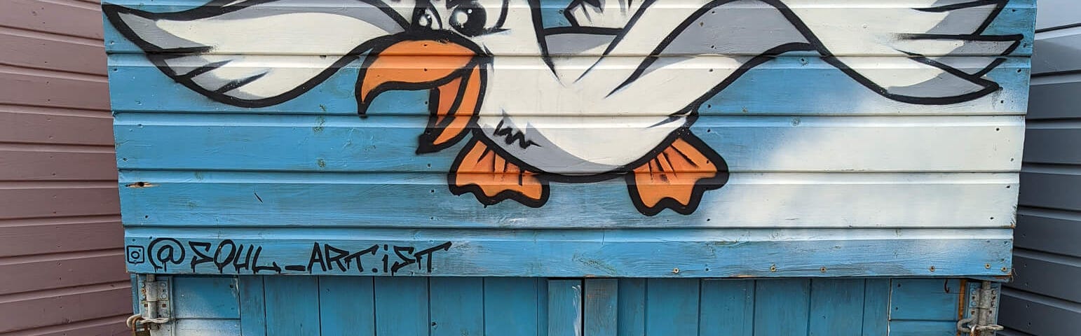 Graffiti on a beach cabin of a sea gull flying over a large portion of french fries. Who wants those french fries more?