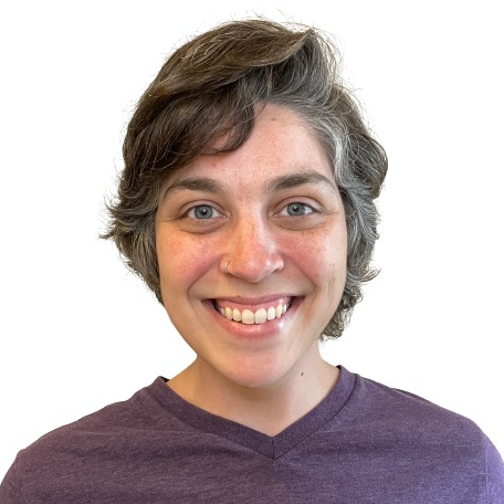 Headshot from the shoulders up featuring Ruth, a blue-eyed androgynous white person wearing wavy short brown hair with gray streaks at the temples, a wide smile exposing their top teeth and gums, and an eggplant purple v-neck t-shirt.