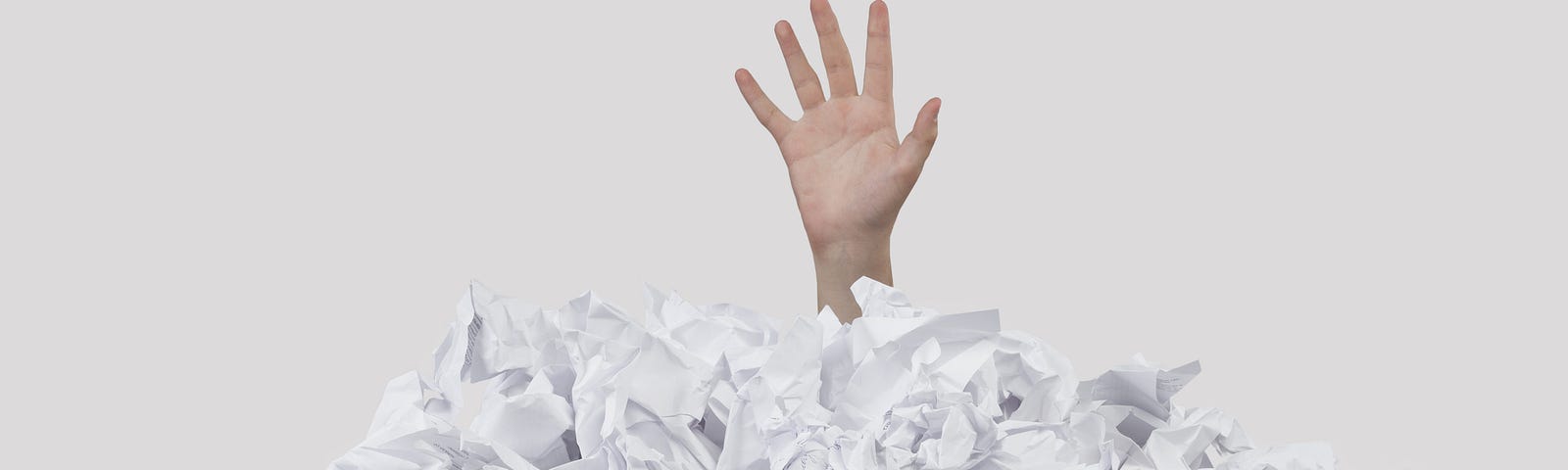 A hand emerging from a pile of scrunched up papers, looking for help