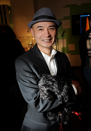 Smiling man wearing a fedora holding a small black dog.