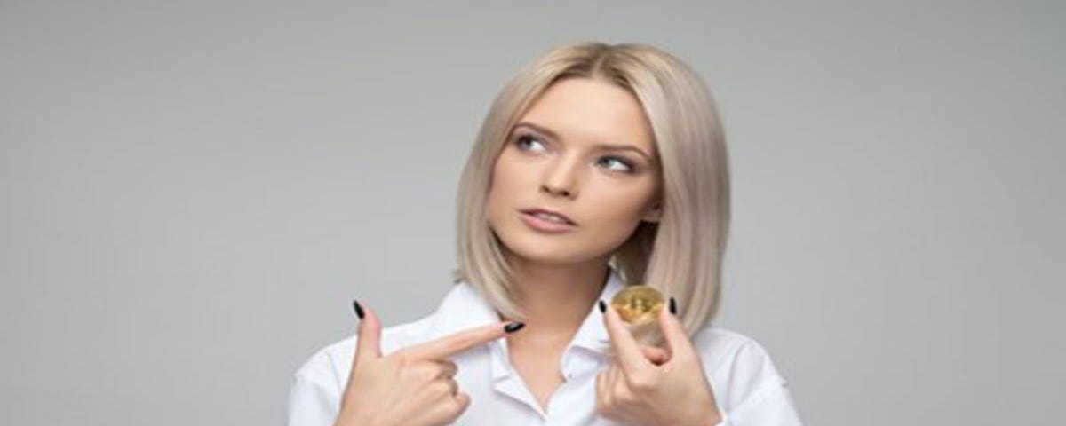 A young lady holding a cryptocurrency in her left hand and pointing to it in her right hand.