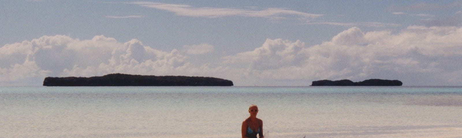 Me sitting on my tandem kayak on the beach with turquoise waters in the background and 2 small islands.