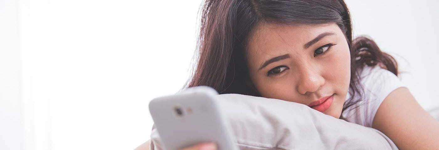 Young woman hugs a pillow as she scrolls her smartphone. She’s visibly bothered.