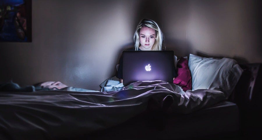 Woman with blond hair working on a laptop in bed