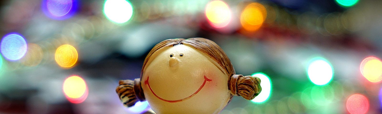 Figurine of a smiling angel holding a golden heart, with a lighted Christmas tree in the background