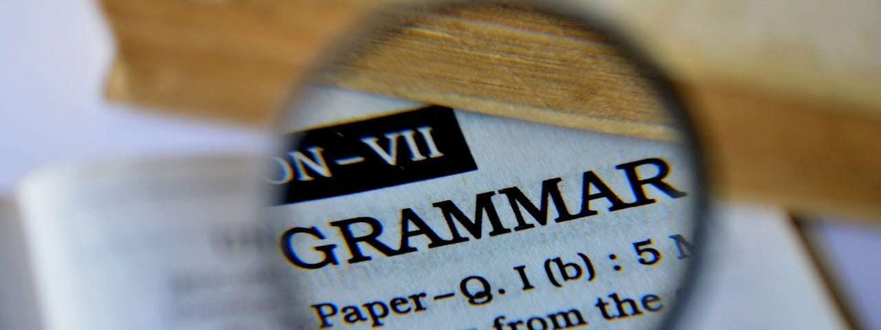 A picture of a magnifying glass magnifying the word “Grammar” in a book