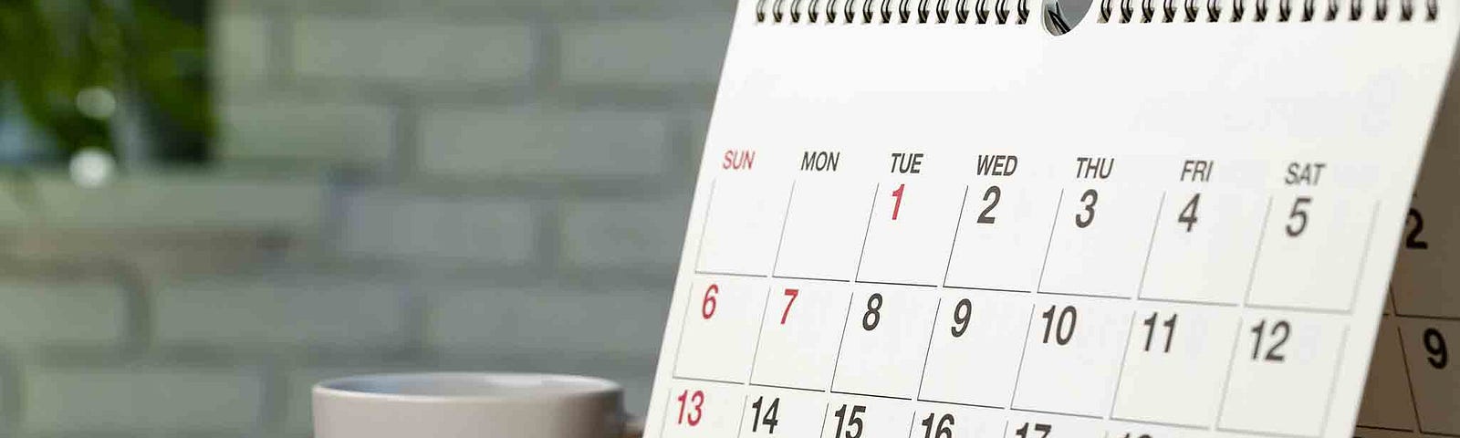 Unmarked calendar propped up on a desk, next to pen, paper, glasses and coffee mug.