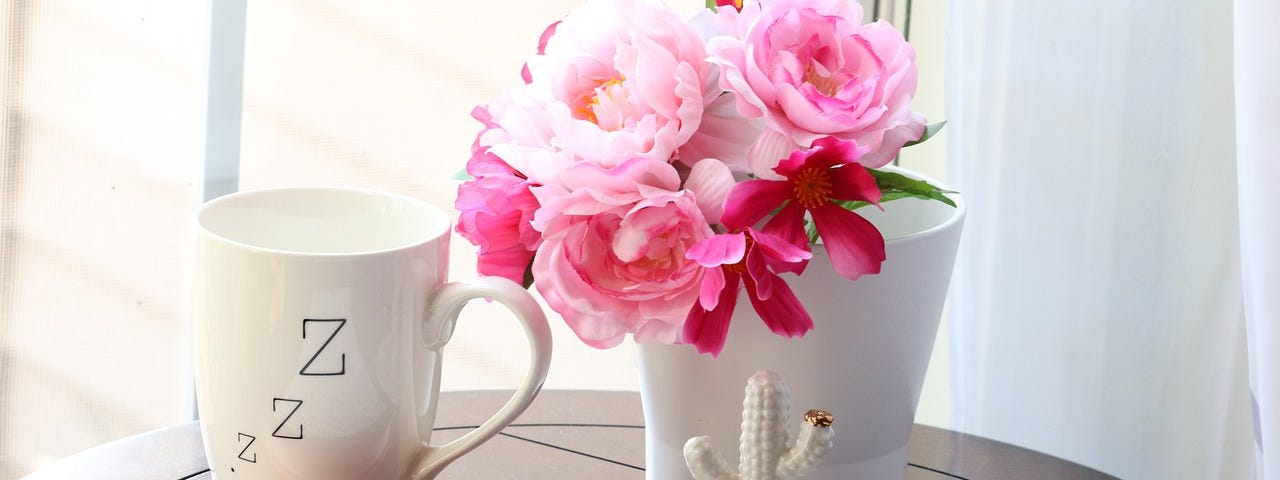 A round table with a bouquet of flowers, a cup of tea and a journal.