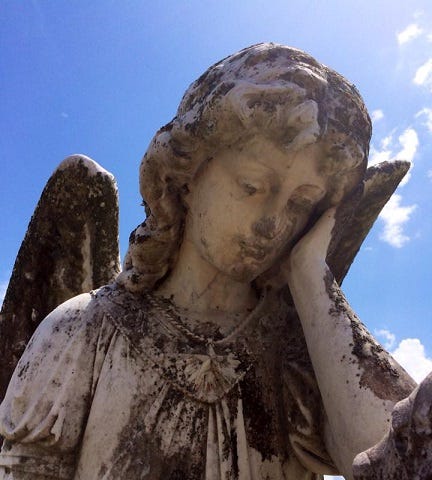 Concrete angel holding her head in one hand, deep blue skies with puffy white clouds behind her