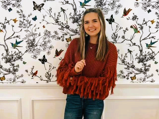 Image of a young woman with long blondish brown hair, wearing a red sweater with blue jeans