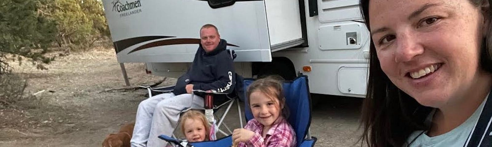 A woman and man sitting outside of an RV with their kids.