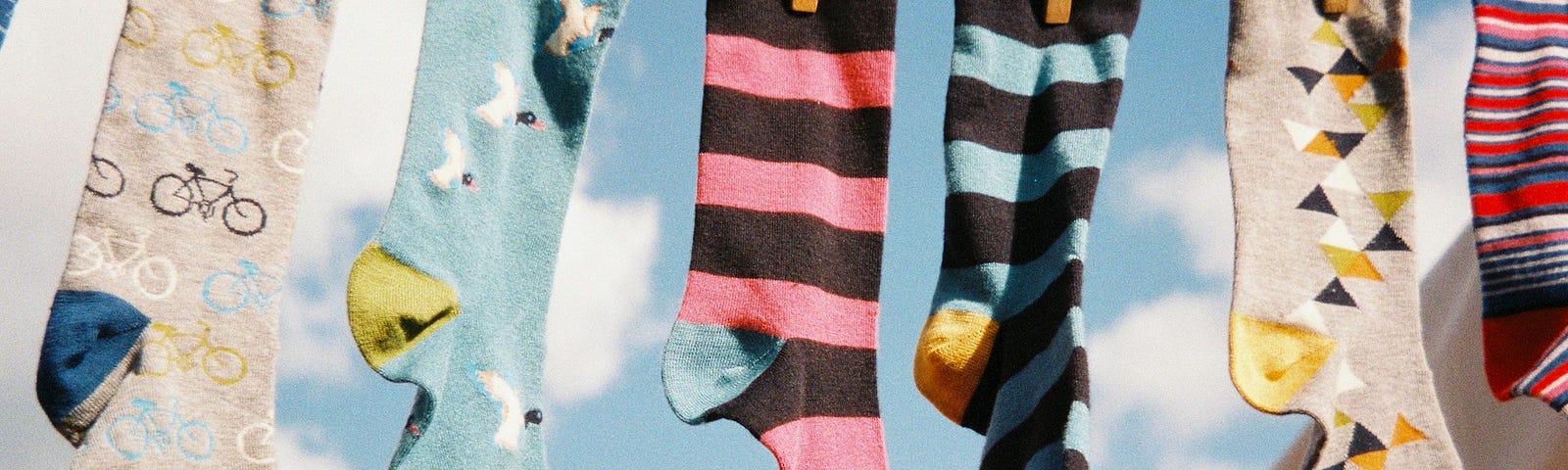 Colourful, patterned socks pegged onto a washing line against a backdrop of blue sky and clouds.