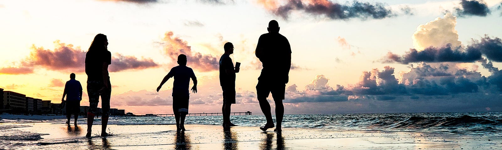 A family walks on a sunset beach in shadow.