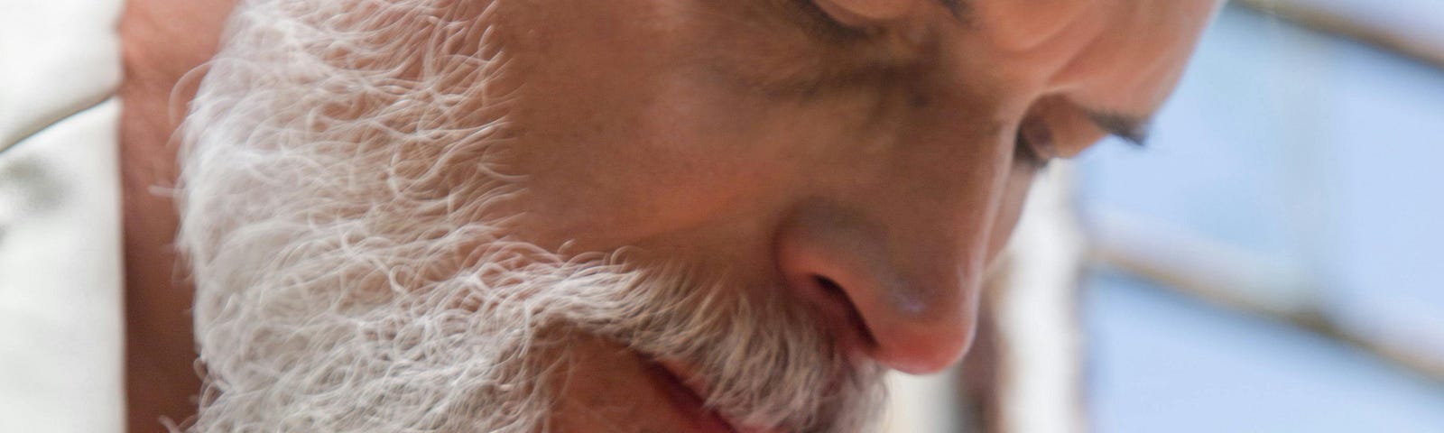 An older man sniffing a flower.