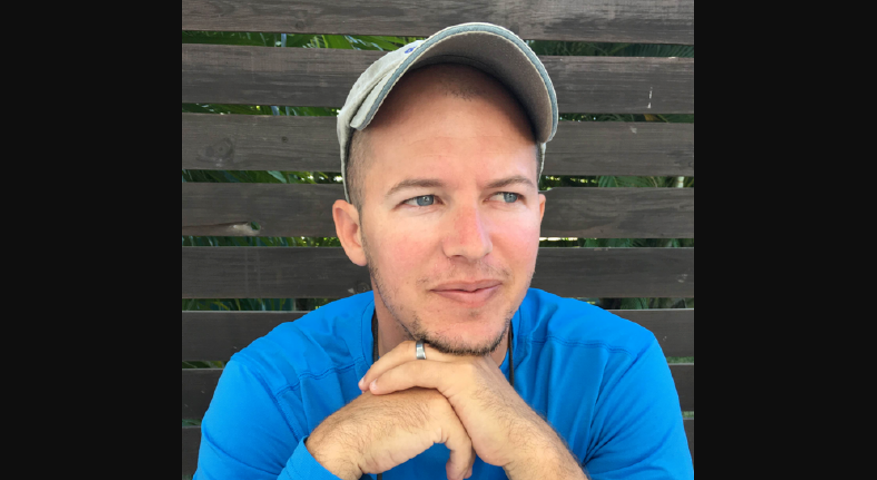 Portrait photo of Jeff Delaney sitting with a cap and hands under chin