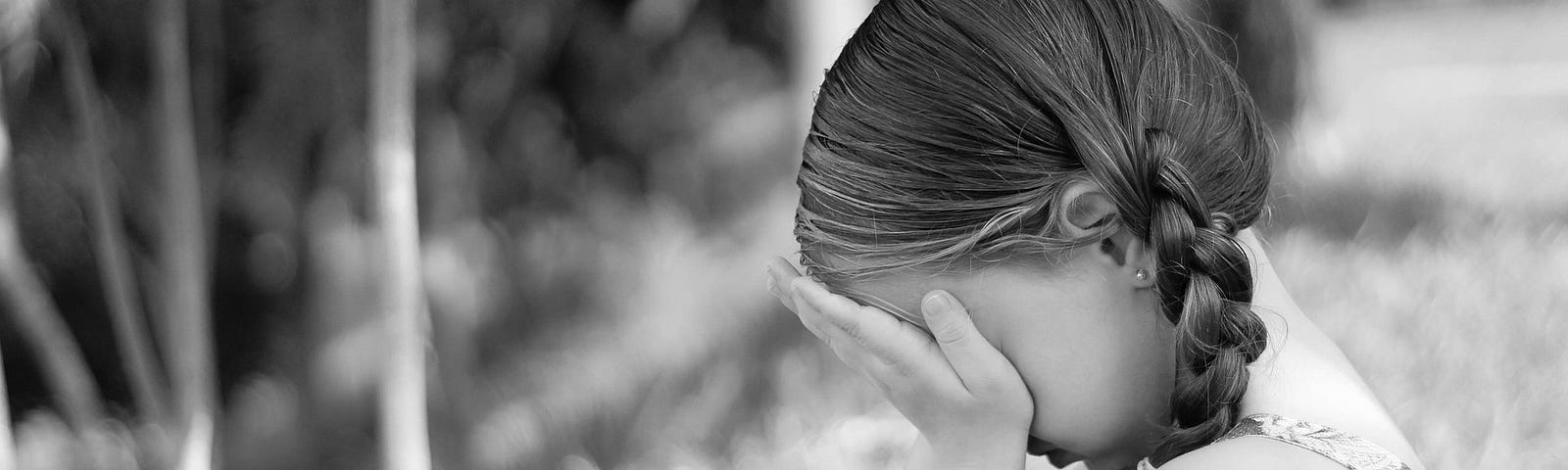 A sad young child hiding their face.