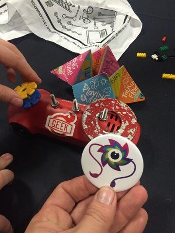 Our colorful mascot “Cal” on a wearable pin/button with a few small, colorful, non-digital games in the background.