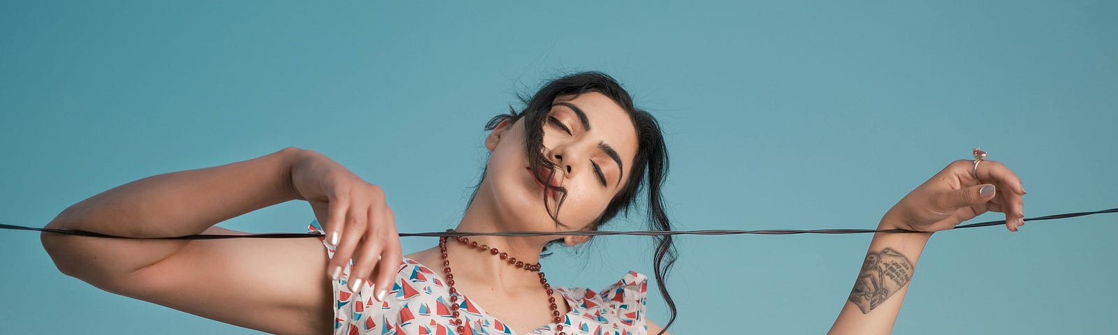 A woman with her eyes closed poses with string against a deep blue sky.