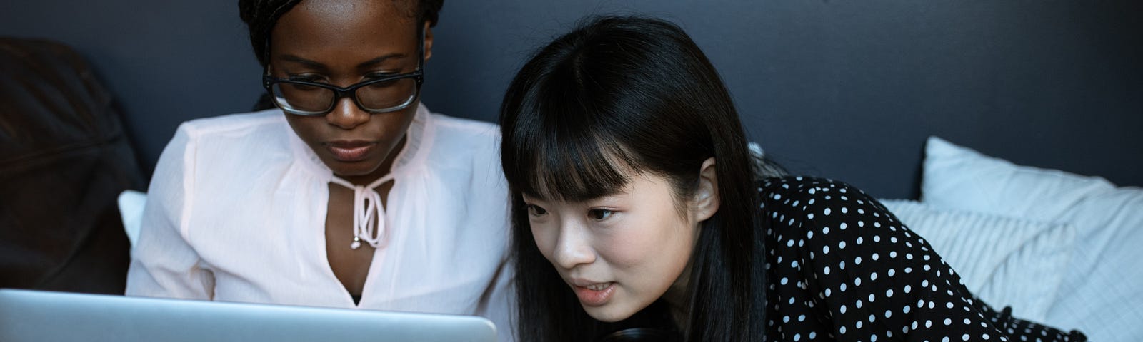 Two women share a laptop screen. They are both in business attire and have a focused look on their faces.