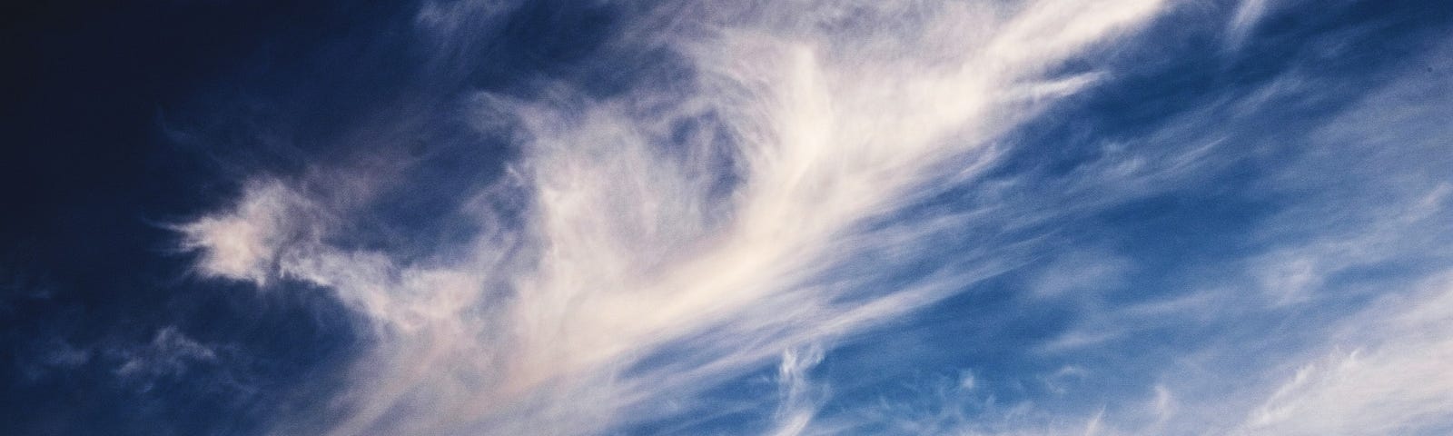 White clouds swept by wind in ocean-blue sky.