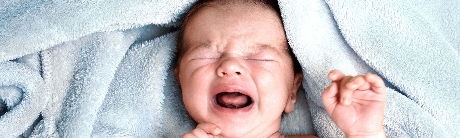 Newborn baby crying while laying on a light blue towel.
