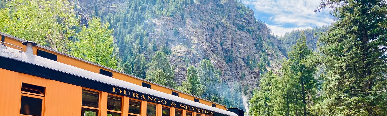 A yellow train car of the Durango-Silverton Railroad sits amidst Colordo mountain scenery