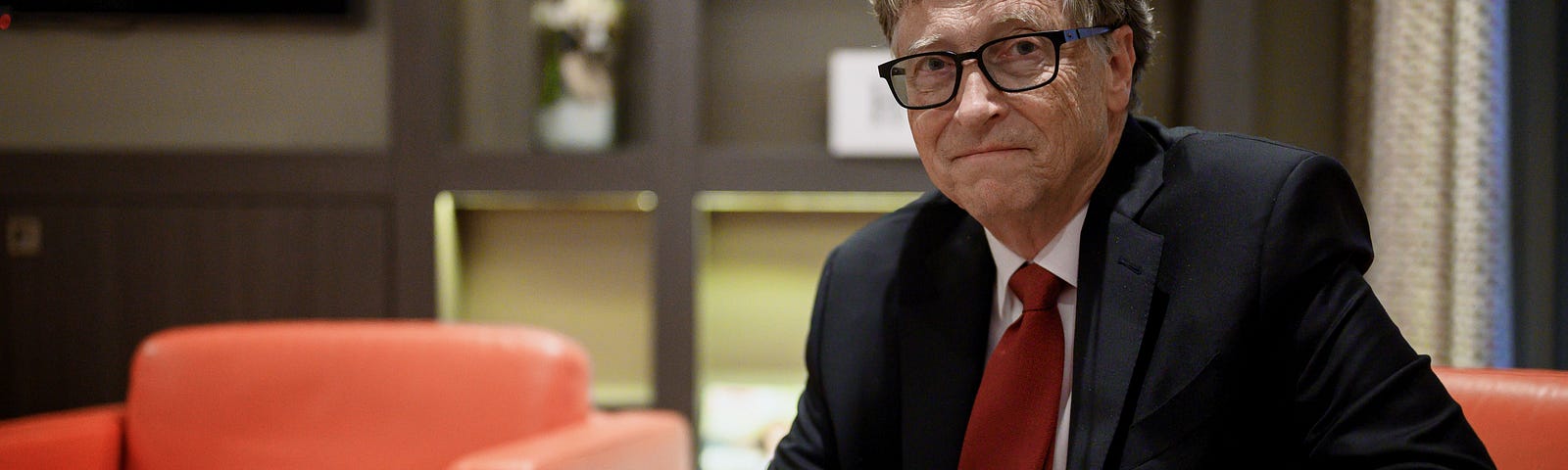 Bill Gates sits on a red armchair and poses for a picture during the funding conference for the Global Fund to Fight AIDS.