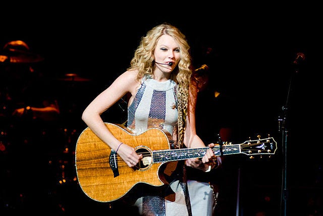 Taylor Swift singing and holding a guitar at a concert.