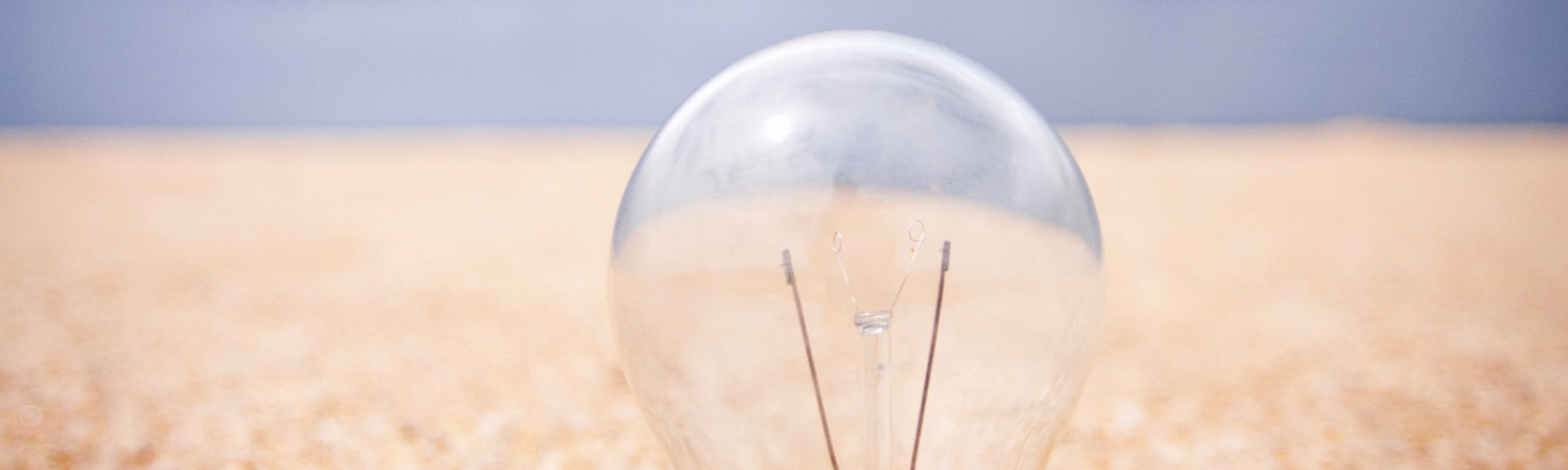 Light bulb in sand with blue sky horizon in the distance.