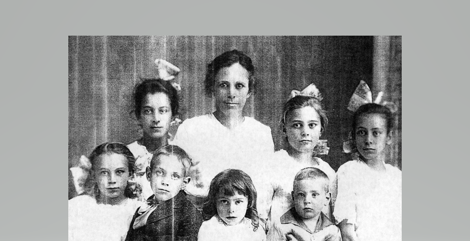 A faded copy of a copy of an old black and white photograph of a backwoods family, a tired, but proud mother in the middle of her brood — posing for the camera — dressed in their “Sunday best” — the five girls with large ribbon bows in their hair, the two boys in suits.