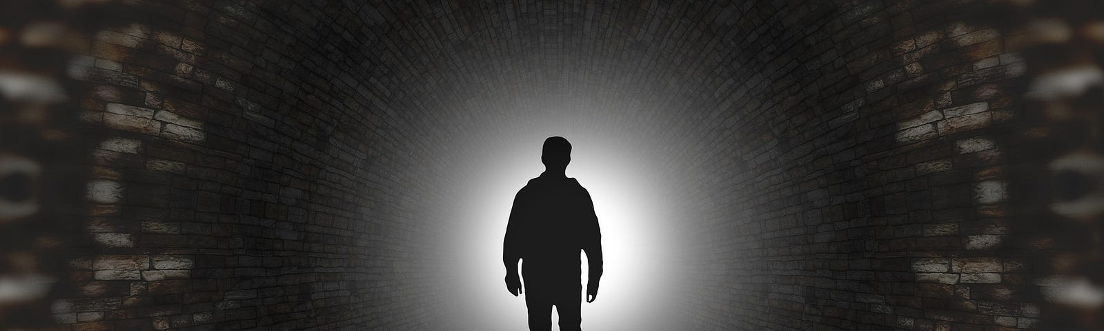 The image is dark, mostly black and shows a person (all black) entering a tunnel where light emanates from the background.