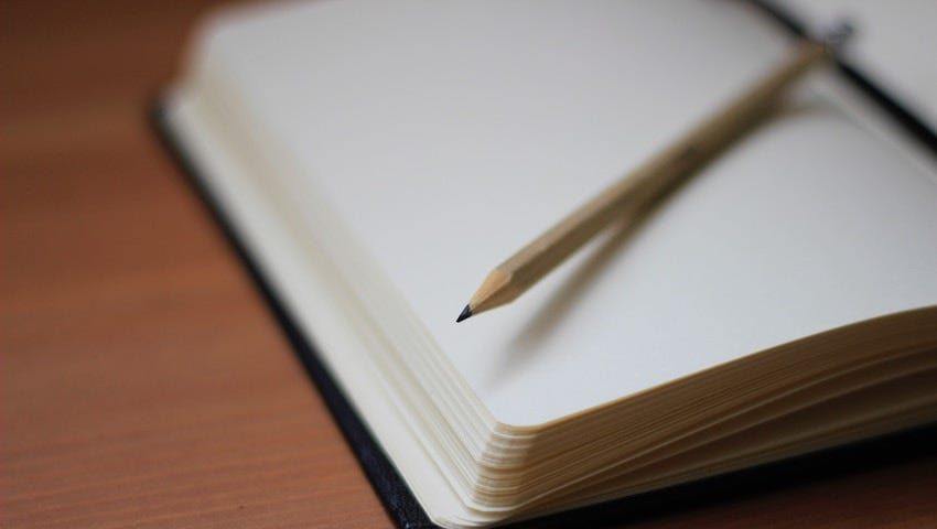 Picture of an empty notebook open, with blank pages. Sharpened pencil on top.