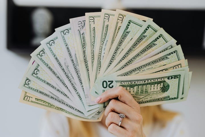 Woman holding cash fanned out in front of her face.