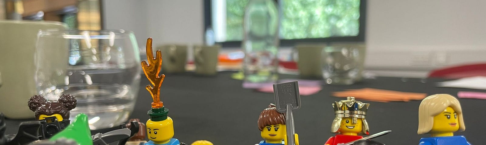 Photo shows oddly dressed lego charactors on a boardroom table in front of a sunny window.