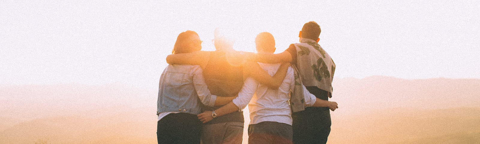 4 people standing, facing the sun hugging each other sideways