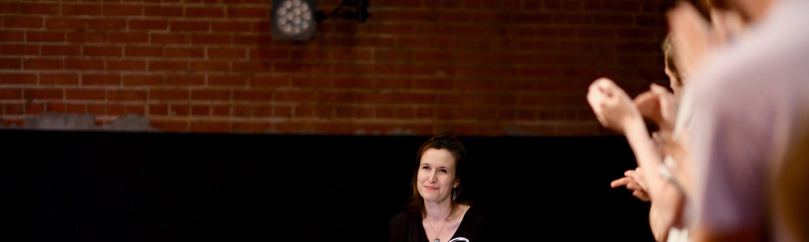 Woman behind keyboard, unfocused audience applauds