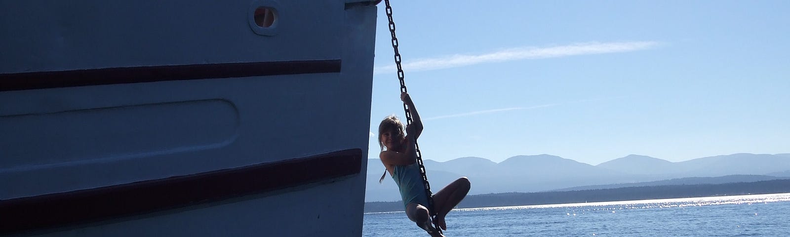 a child climbs up the anchor chain of a boat. A man is watching from the deck of the boat