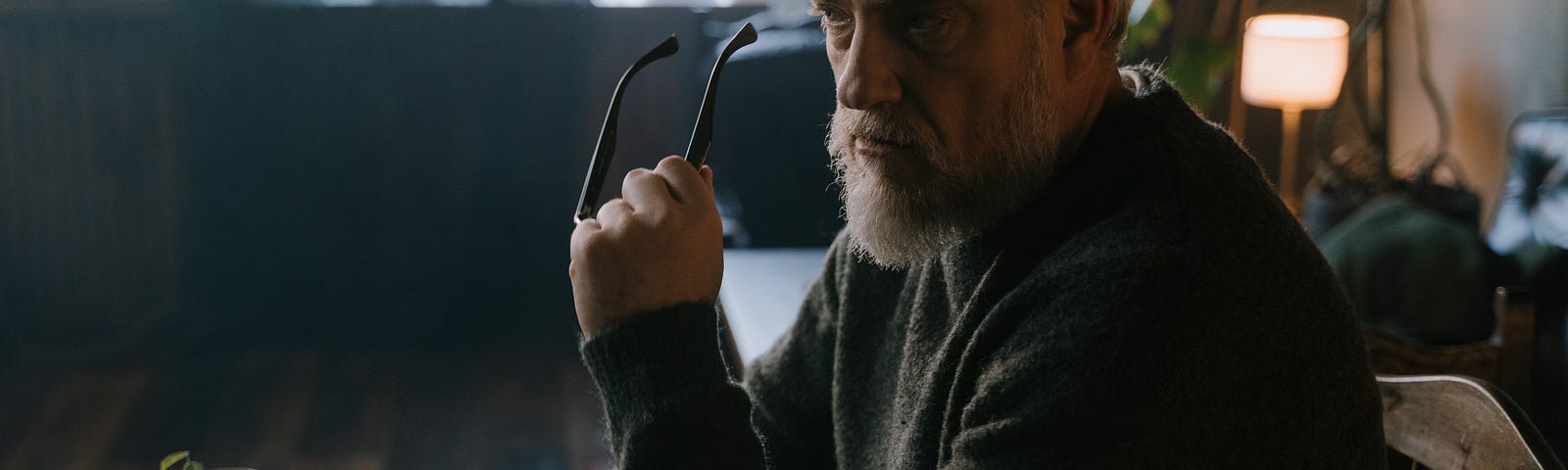 A bearded man holding his glass while sitting with a desk full of papers