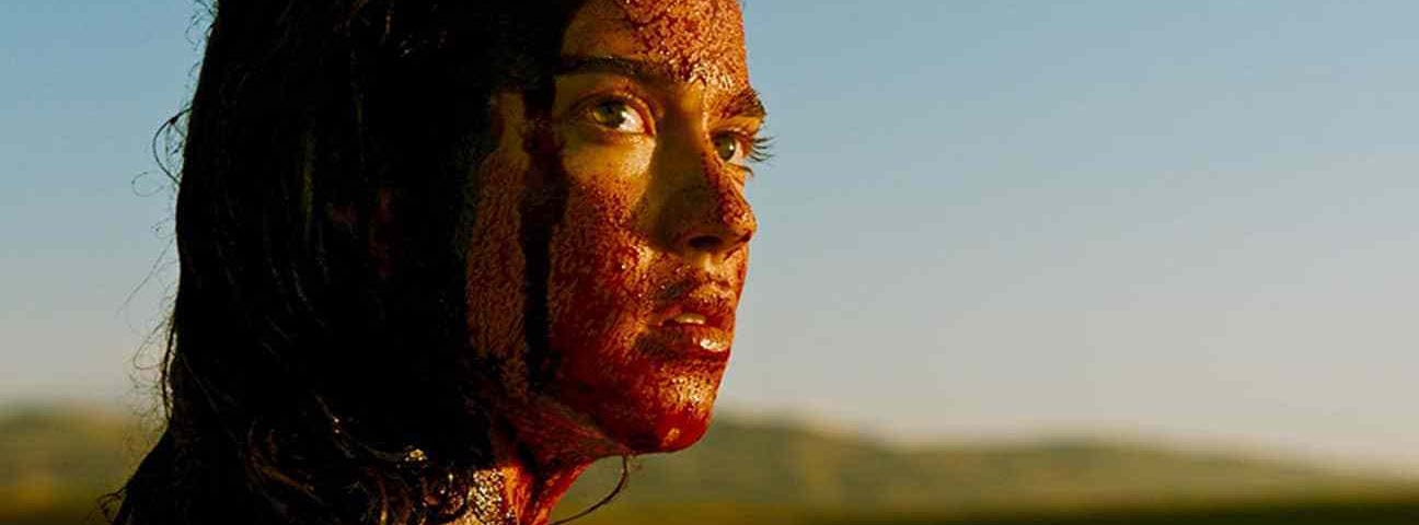 A women covered in blood is seen looking upon her shoulder in a desert.