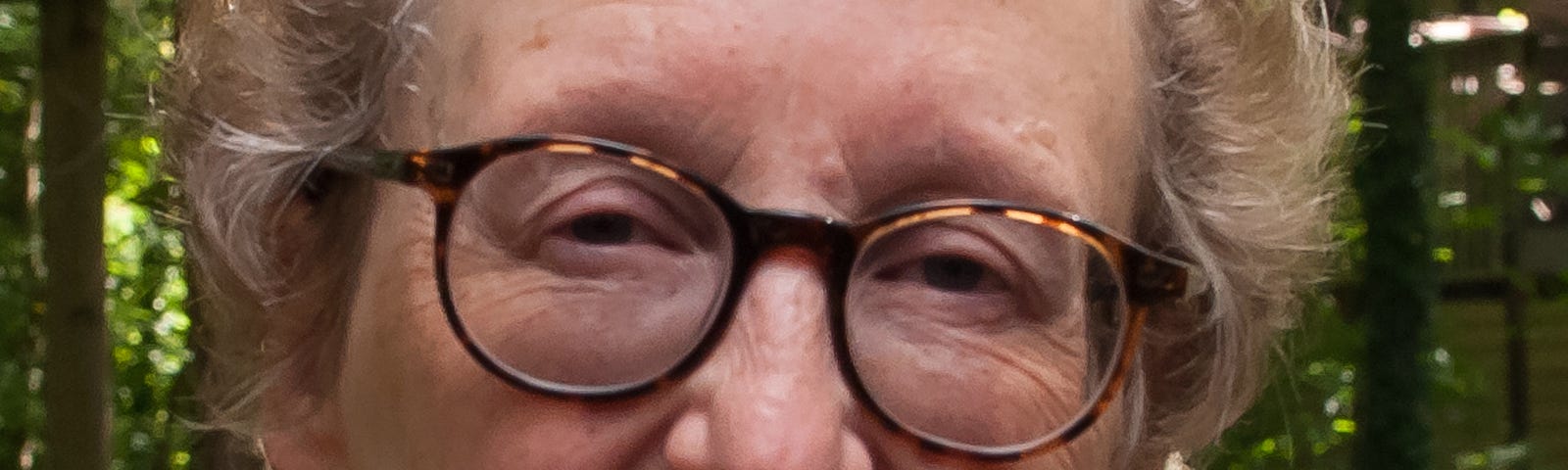 Blonde woman with tortoise-shell glasses, headshot, outdoors.