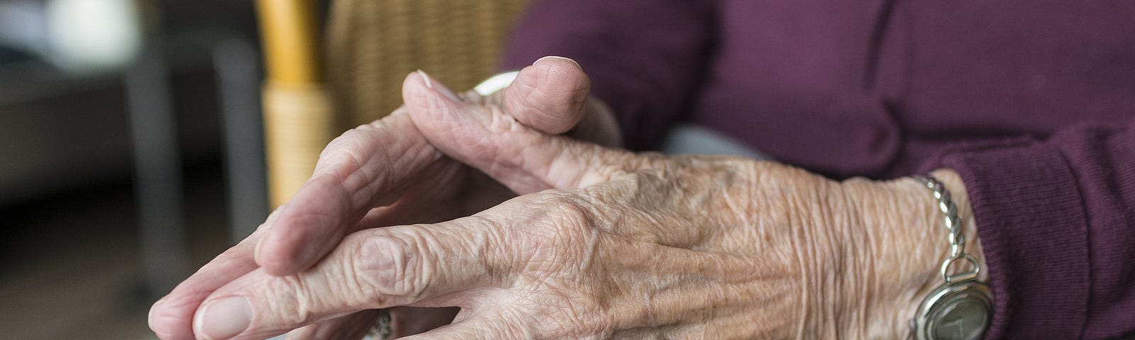 Old woman’s folded hands on her lap.