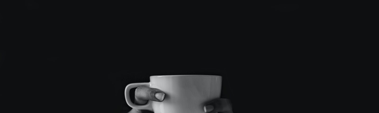 Two hands holding a coffee mug against a black background