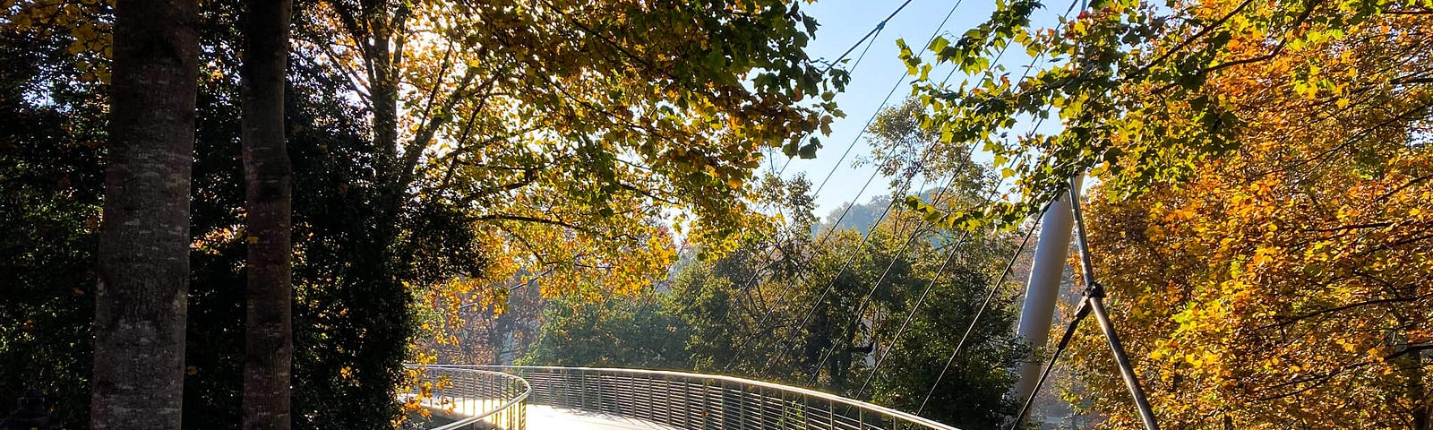 Suspension bridge curving off into the distance with sunshine at end