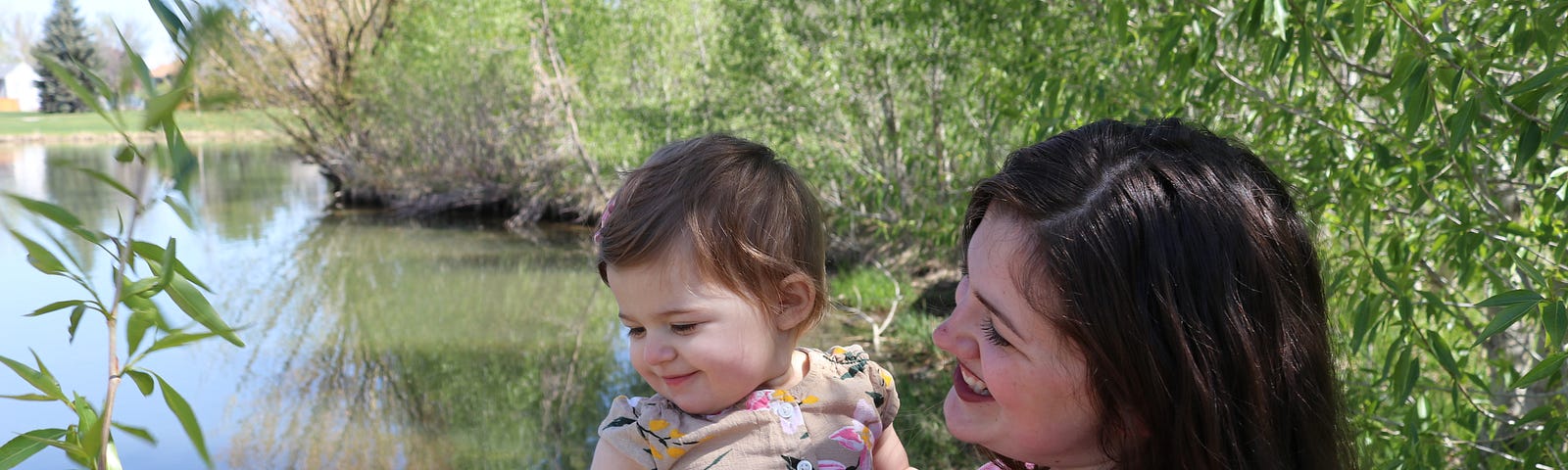 The author holds her infant daughter adjacent a pond in springtime.