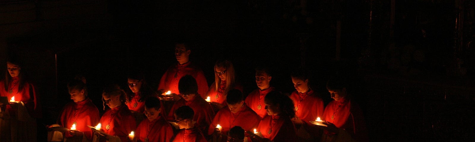 A choir in red robes lighted only by candles they are holding.