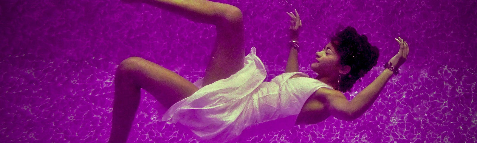 Image of woman wearing a white dress drifting into the unknown. Her arms are outstretched and she is surrounded by purple light.