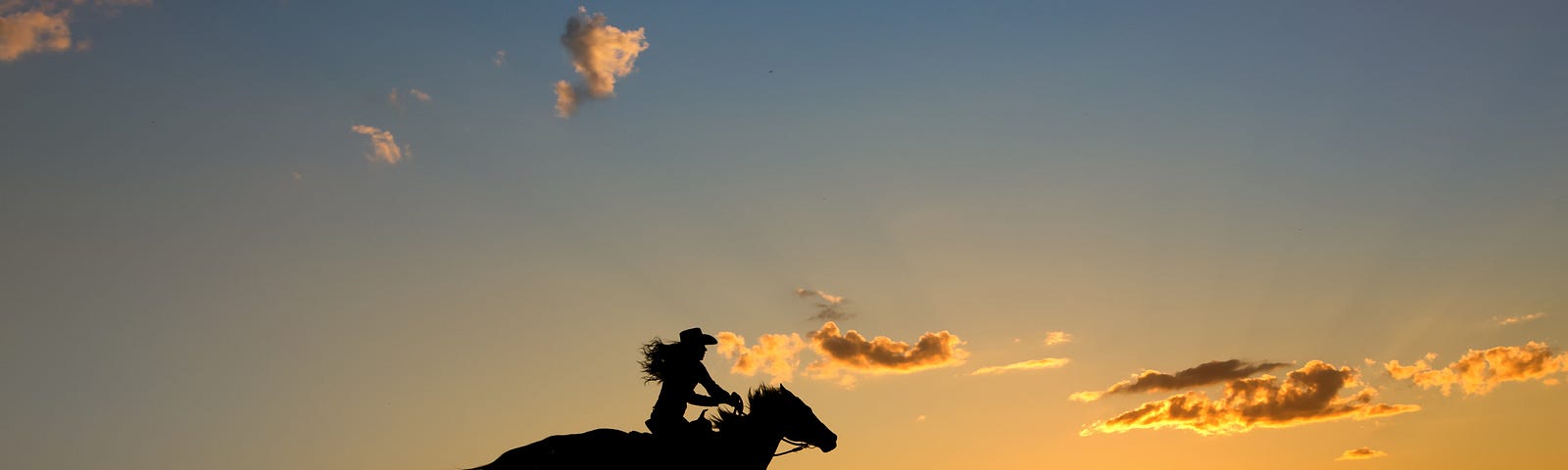 A silhouette of a girl galloping on a horse at sunrise. The horse has his mane and tail flying.