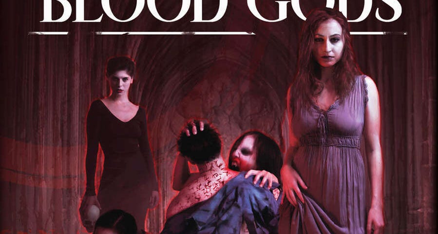 The book cover shows the title, Cults of the Blood Gods, in bold white text at the top. Below is a scene of 4 female vampires and a human male. Two are drinking his blood, one from his neck, one from his wrist. A third woman with read hair and a simple purple dress stands in the foreground looking at the camera. A forth woman, with short black hair and a long black gown, stands in the background also looking at the camera. They appear to be in some sort of church.